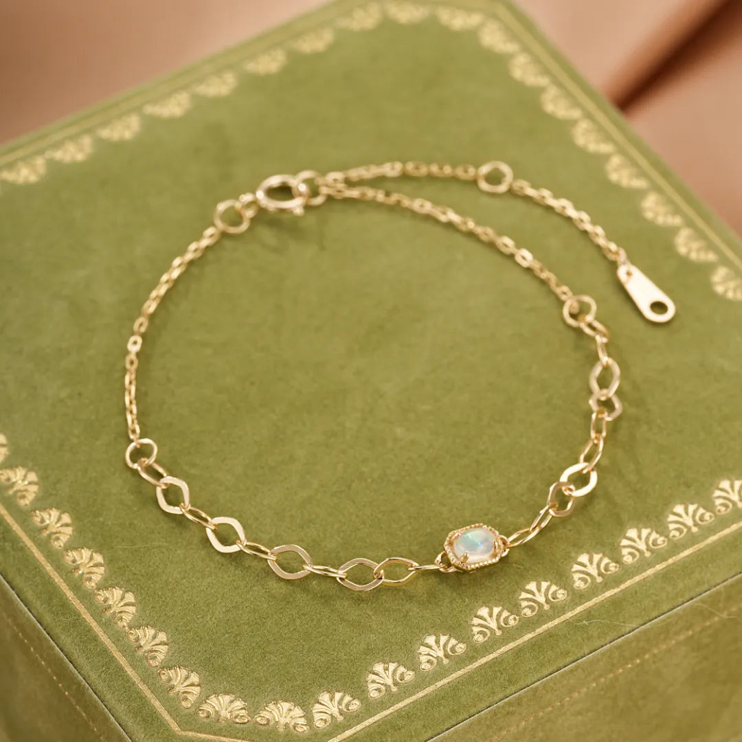 Bracelet fin en argent doré à l'or avec une opale ovale au centre, monté sur une chaîne à maillons entrelacés.
