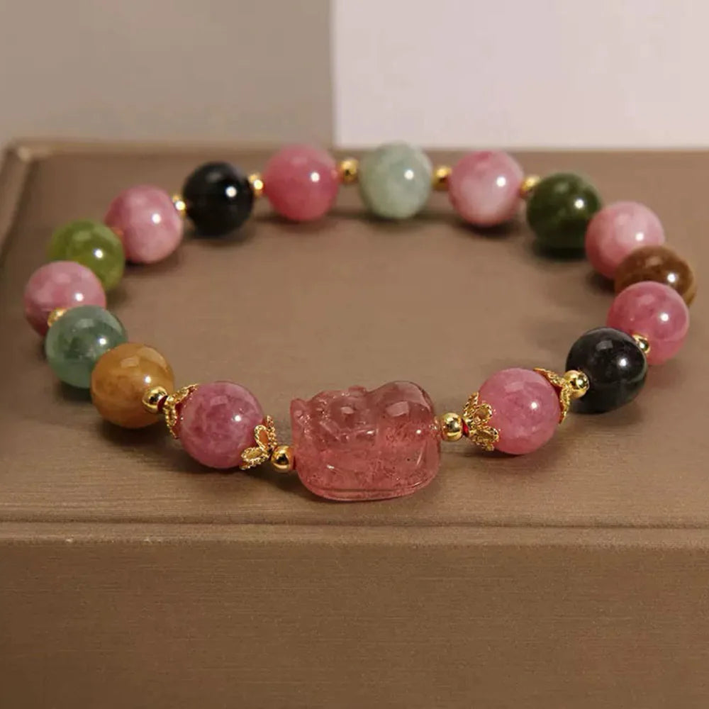 Bracelet Pi Xiu en tourmaline et quartz fraise, orné de perles multicolores et de détails dorés. La pièce centrale est une sculpture de Pi Xiu translucide rose.