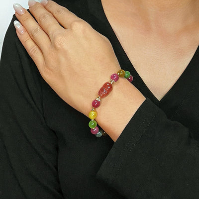 Bracelet "Richesse Spirituelle" en tourmaline et quartz fraise avec une breloque Pi Xiu rouge au centre, porté au poignet d'une femme.