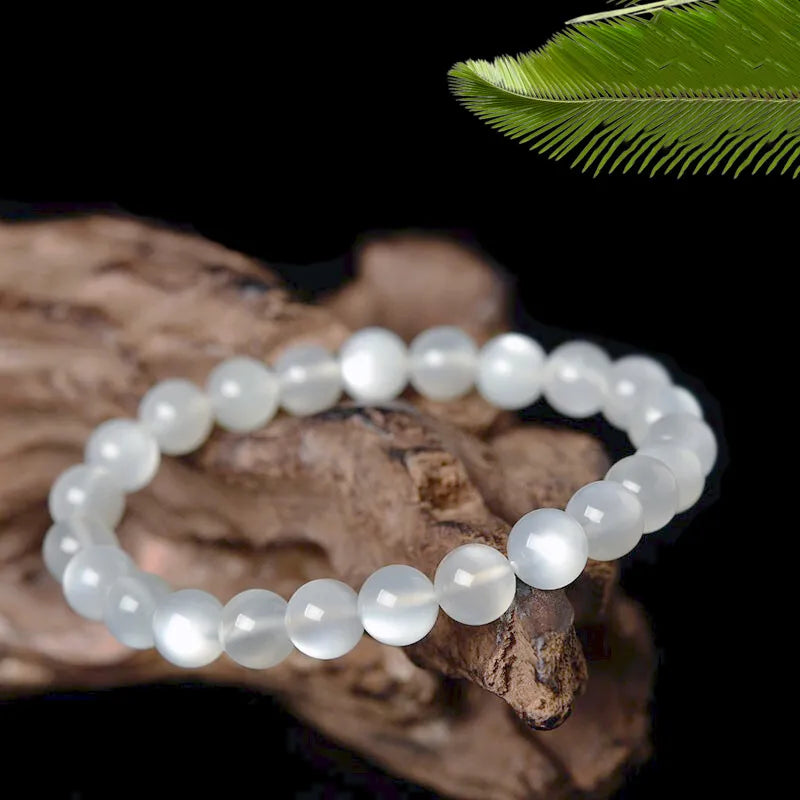 Bracelet en pierres de lune blanches facettées, bijou "Élégance Lunaire" sur un support en bois avec une feuille de palmier en arrière-plan.