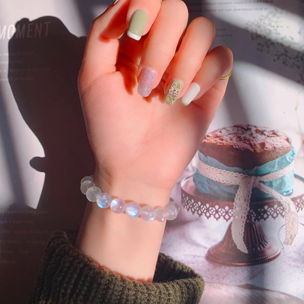 Bracelet "Rêve Doux" en pierres de lune naturelles montées sur élastique, porté au poignet, avec un premier plan flou sur un gâteau décoré.