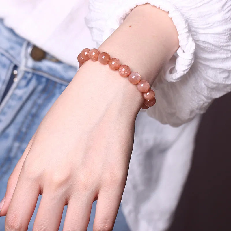 Bracelet en pierre de soleil aux teintes orangées, monté sur un fil élastique, porté au poignet d'une personne.