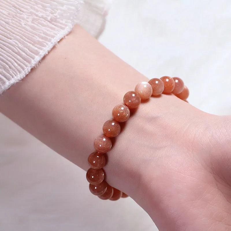 Bracelet "Élégance Solaire" fait de perles rondes en pierre de soleil orange vif, porté au poignet d'une personne.
