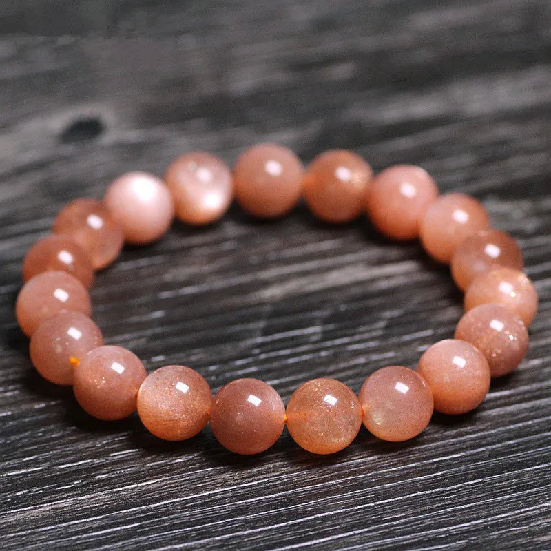 Bracelet "Élégance Solaire" fait de perles rondes de pierre de soleil orangée, posé sur un fond en bois sombre.