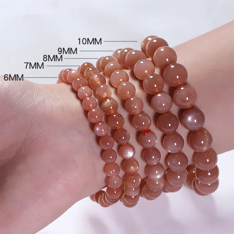 Plusieurs bracelets de perles de pierre de soleil de différentes tailles (6mm, 7mm, 8mm, 9mm, 10mm) enfilés sur un poignet, montrant la variation de taille des perles.