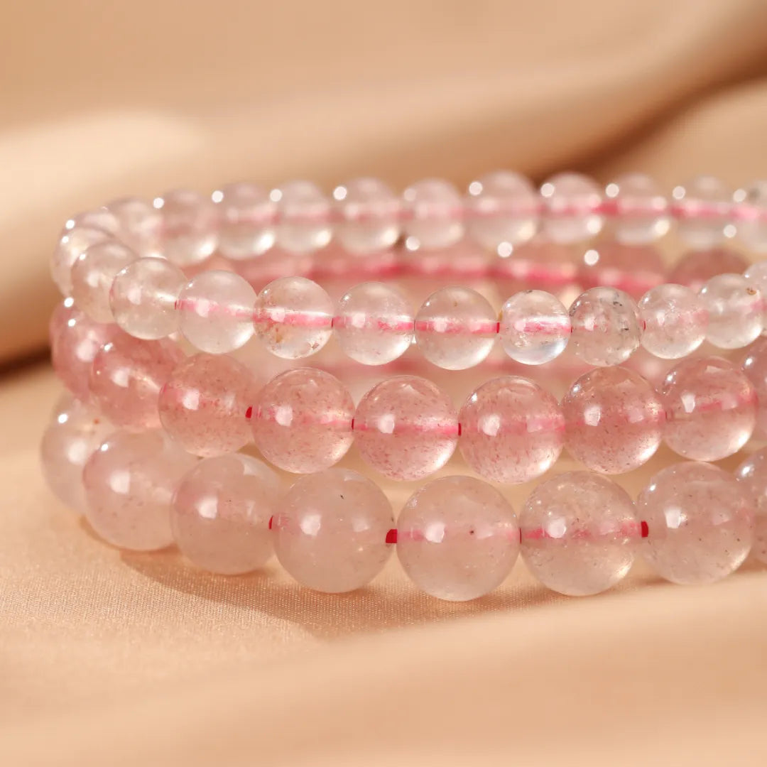 Lot de trois bracelets en quartz fraise "Rose Doux" aux perles rondes translucides roses et blanches, enfilées sur un fil élastique rouge.