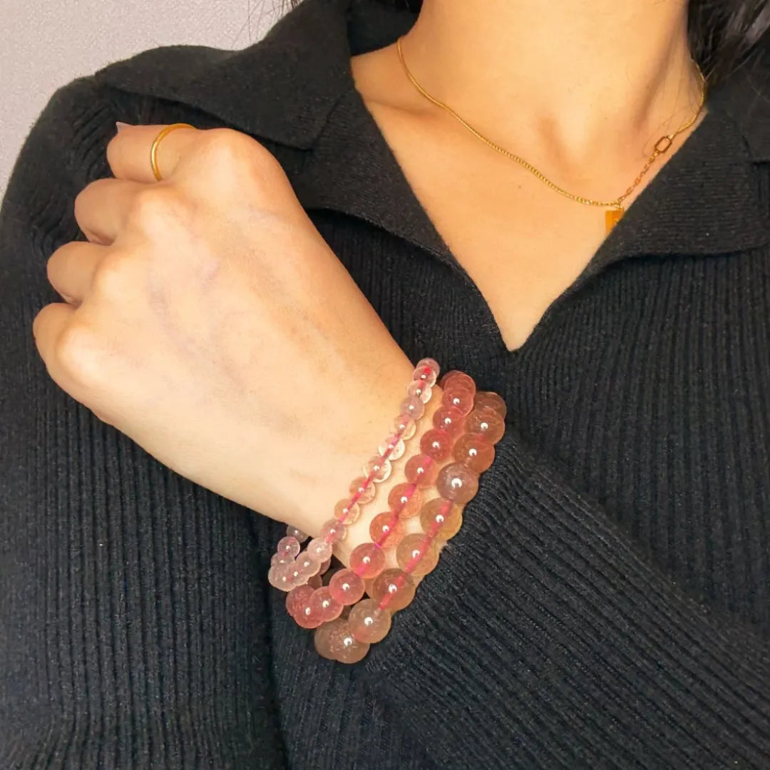 Trois bracelets en quartz fraise rose doux portés au poignet d'une femme, avec une bague dorée et un collier fin.