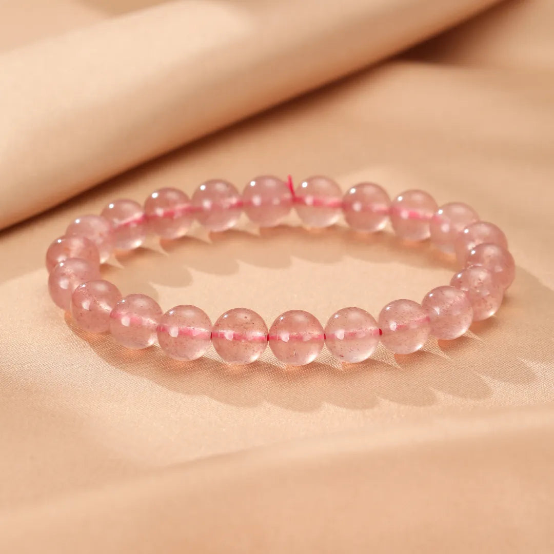 Bracelet en quartz fraise "Rose Doux" avec des perles rondes roses translucides enfilées sur un fil rouge.