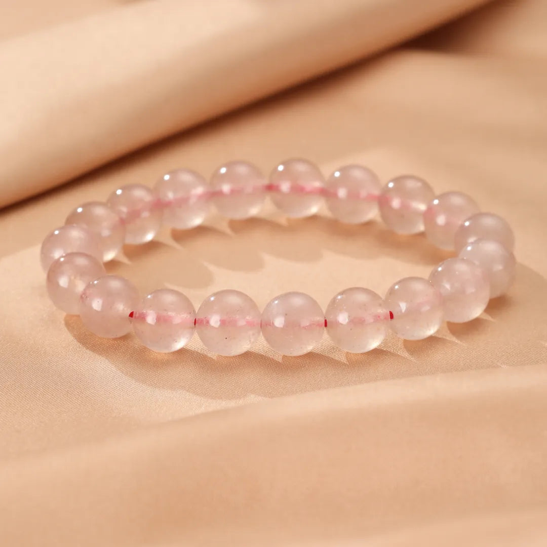Bracelet "Rose Doux" en quartz fraise, avec des perles rondes roses translucides et une fine ficelle rose visible entre les perles, posé sur un tissu satiné beige.
