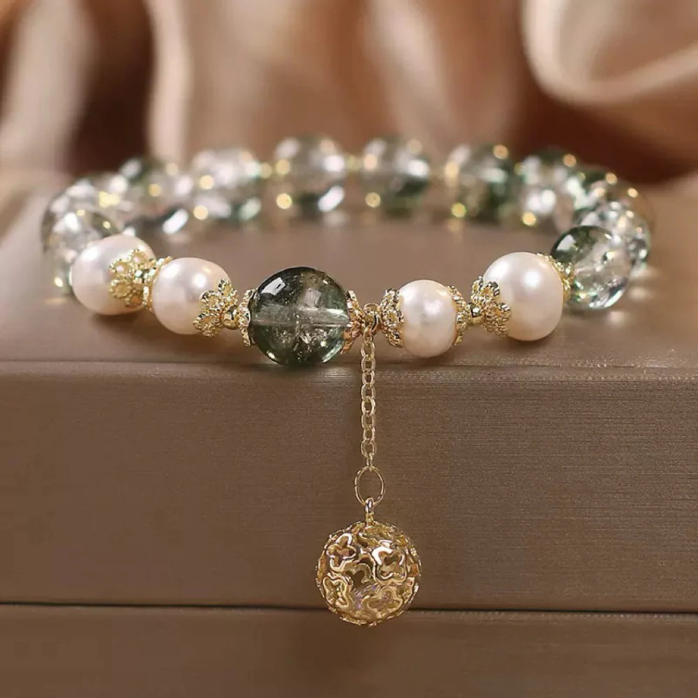 Bracelet en quartz vert et perles blanches avec une breloque sphère dorée ajourée.