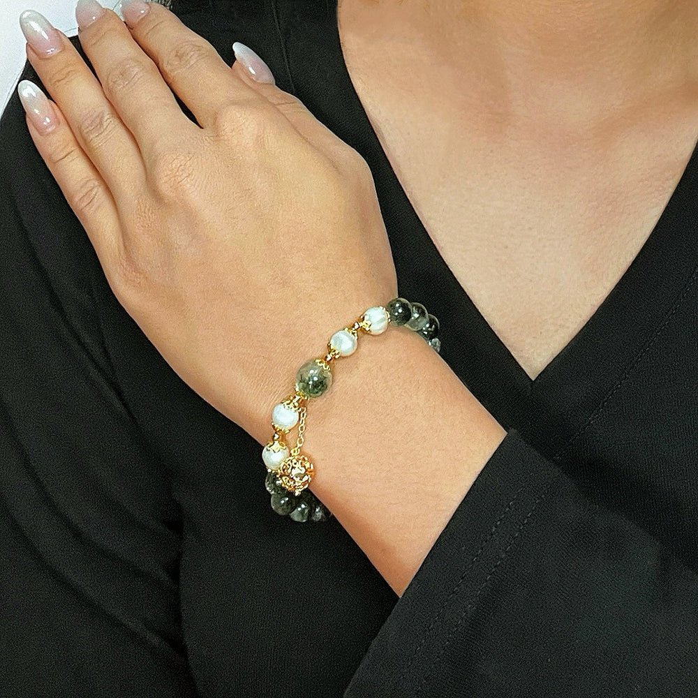 Bracelet en quartz vert et perles blanches, orné d'une perle centrale dorée sphérique, porté au poignet d'une femme.