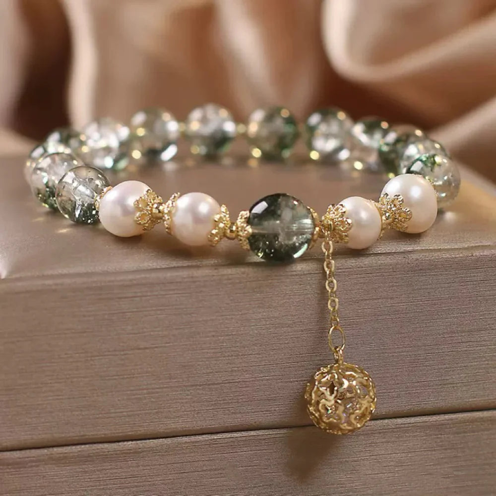 Bracelet en quartz vert et perles nacrées avec un pendentif sphère dorée ajourée, monté sur une chaîne fine.