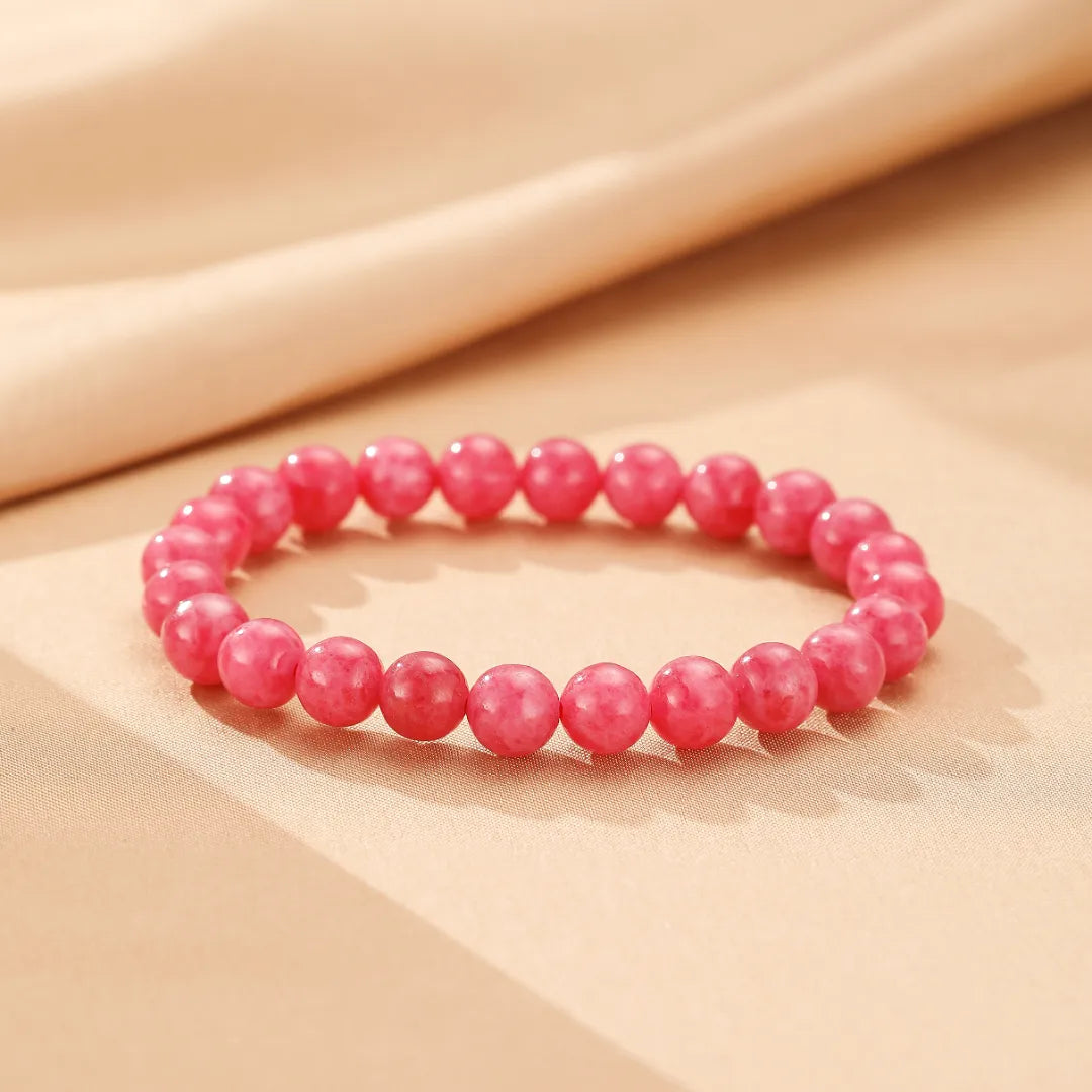 Bracelet en rhodonite avec des perles rondes d'un rose tendre, disposé sur un fond clair avec des plis doux.