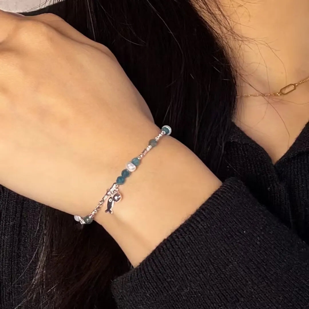 Bracelet "Charme Poisson" en argent 925 avec des pierres topaze bleues et des perles blanches, orné d'un pendentif poisson argenté.