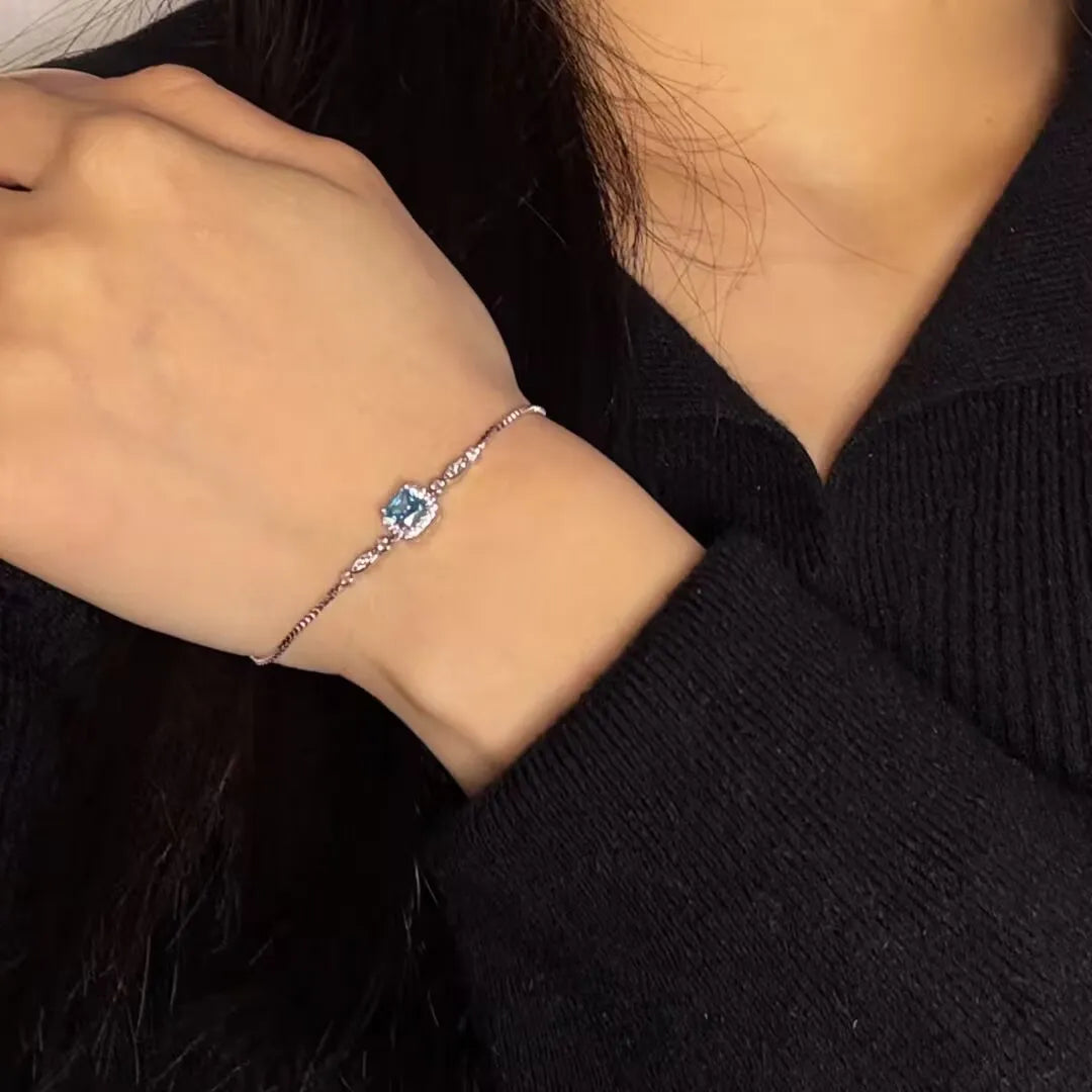 Bracelet "Magie Océanique" en argent 925 avec une topaze bleue carrée entourée de petits cristaux, porté au poignet.