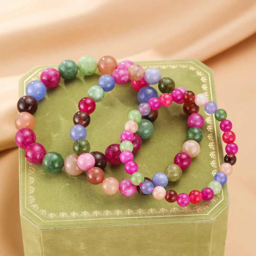 Deux bracelets en pierres naturelles de tourmaline multicolores, rose, bleu, vert et violet, sur une boîte cadeau verte.