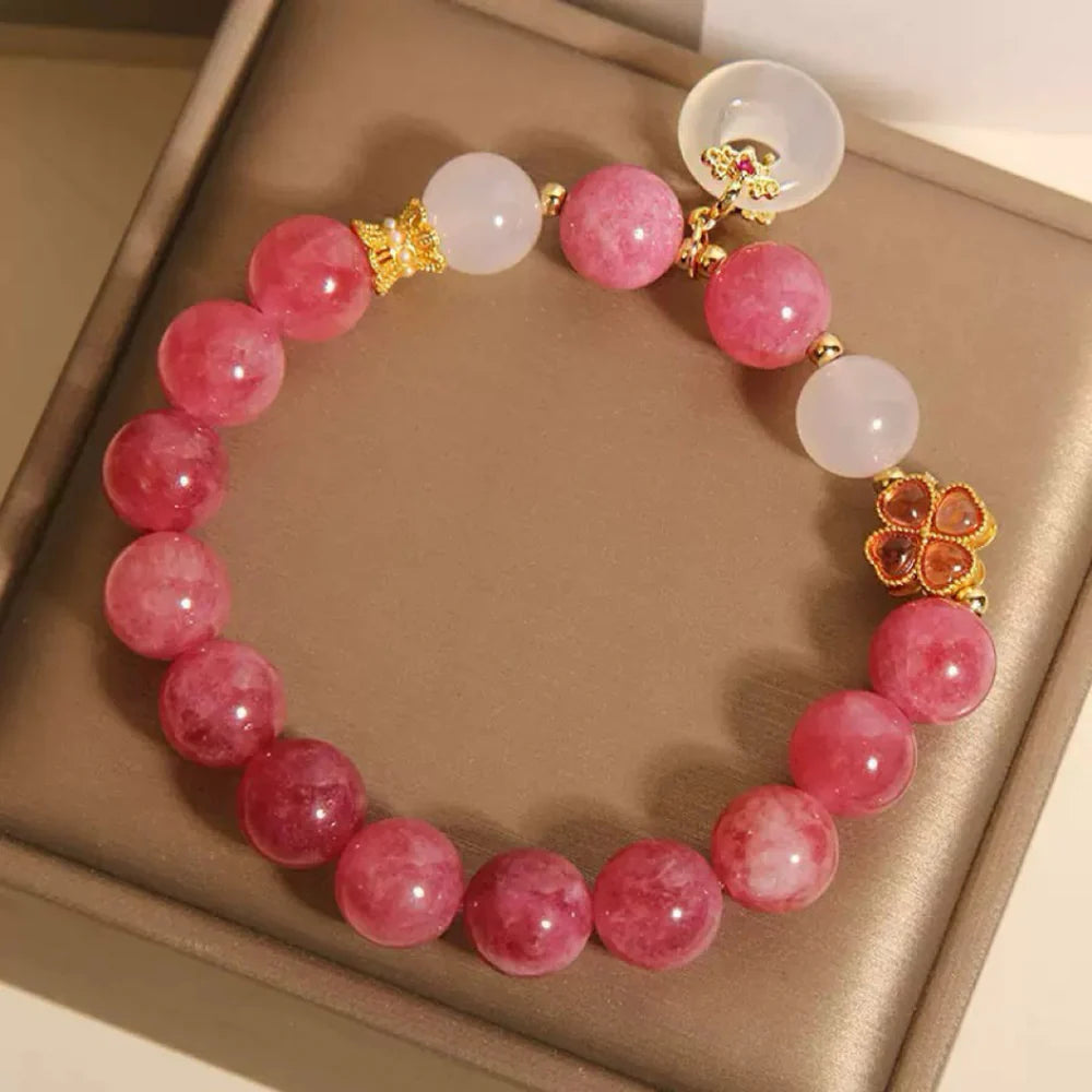 Bracelet "Douceur Éclatante" orné de perles de tourmaline rose et de jade blanc, avec un pendentif trèfle doré et une pierre translucide.