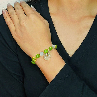 Bracelet Trèfle Tourmaline Verte et Jade "Rayons d'Optimisme" porté au poignet d'une femme, orné de perles vertes et blanches et d'une breloque de jade.