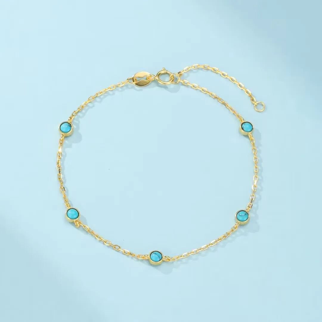 Bracelet en argent doré avec chaîne fine et petites pierres turquoise rondes disposées tout autour sur fond bleu clair
