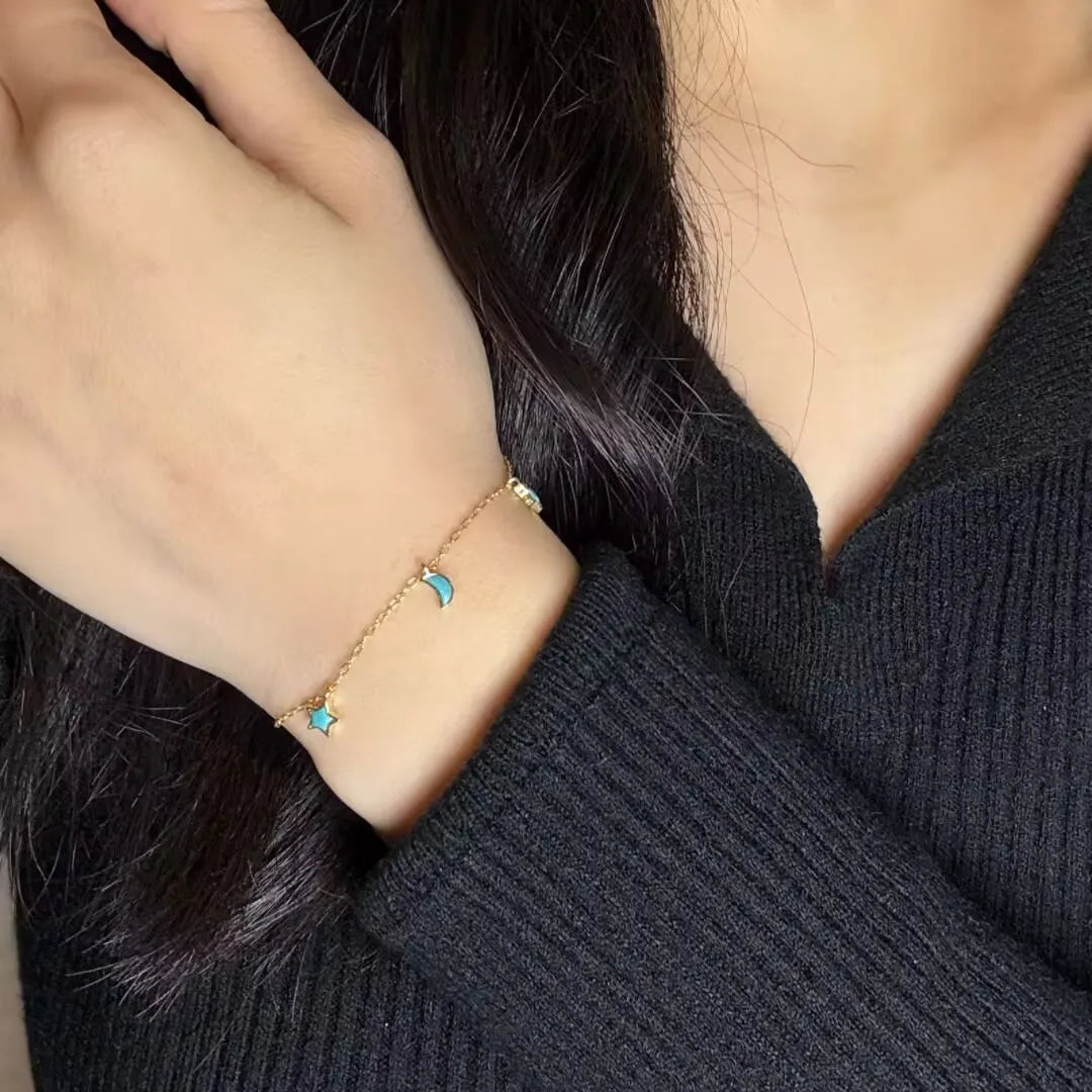 Bracelet fin en argent doré or, orné d'une turquoise en forme d'étoile et d'une turquoise en forme de lune, porté au poignet d'une femme.