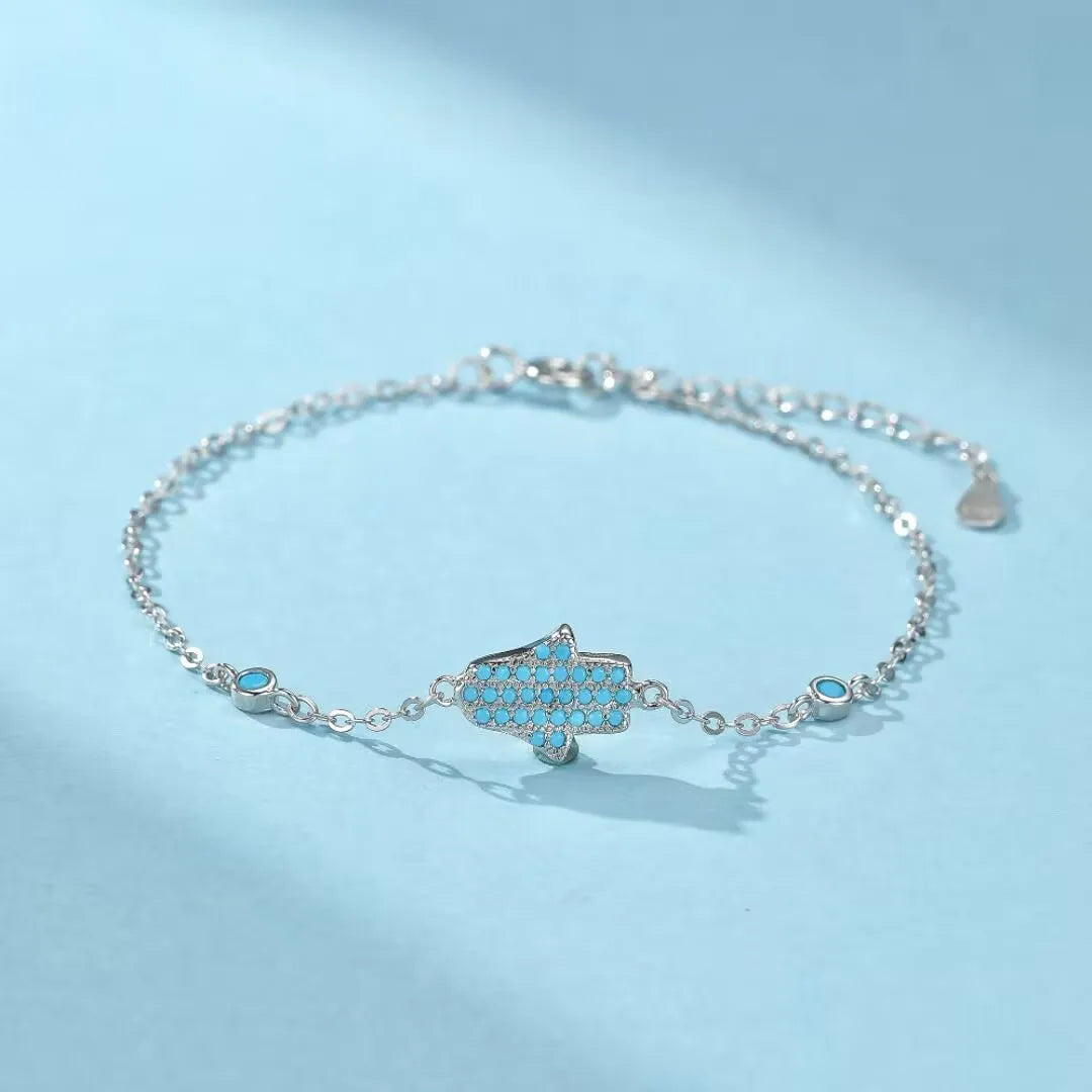 Bracelet "Perle Protectrice" en argent 925 orné d'une main de Fatma sertie de turquoises et de petites pierres bleues sur une chaîne fine.