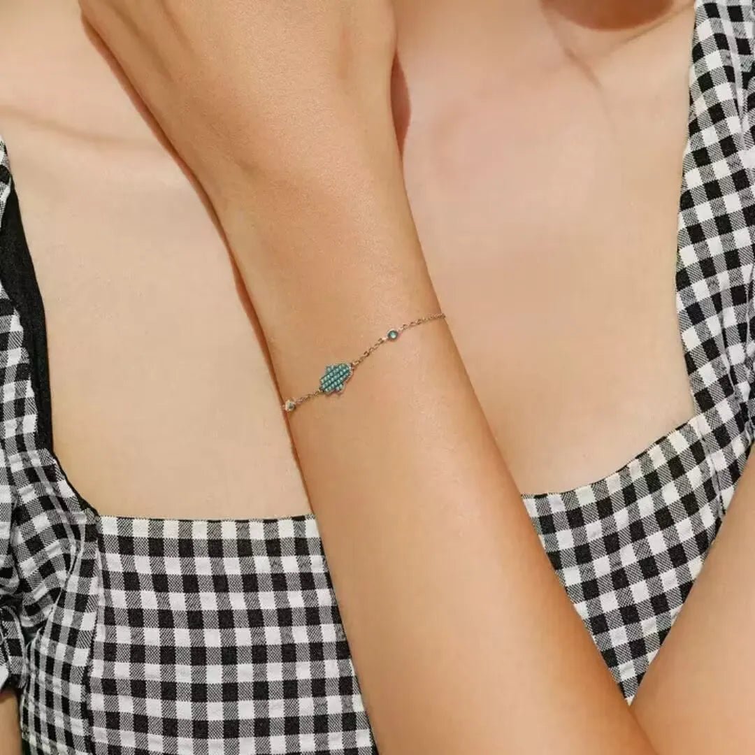 Bracelet fin en argent 925 avec une main de Fatma turquoise incrustée de petites pierres bleues et blanches.