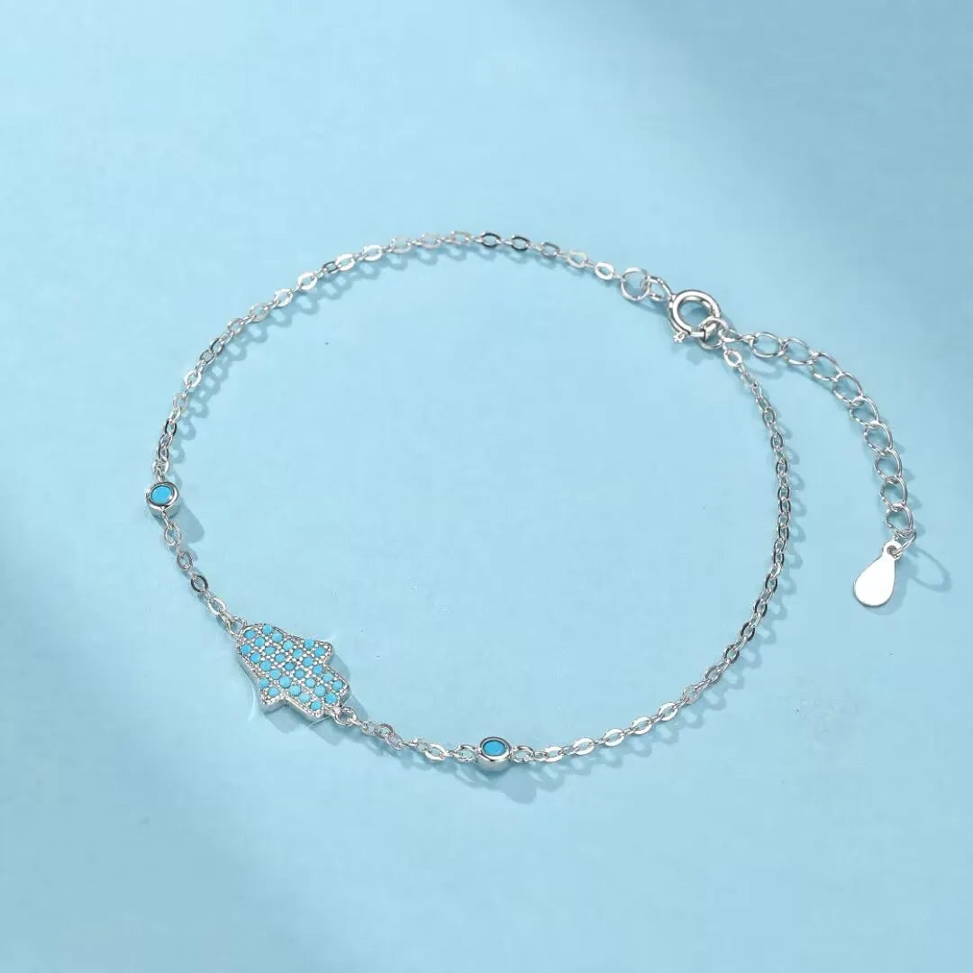 Bracelet "Perle Protectrice" en argent 925 orné d'une main de Fatma sertie de turquoise et de petites pierres bleues, avec une chaîne fine et un fermoir ajustable.