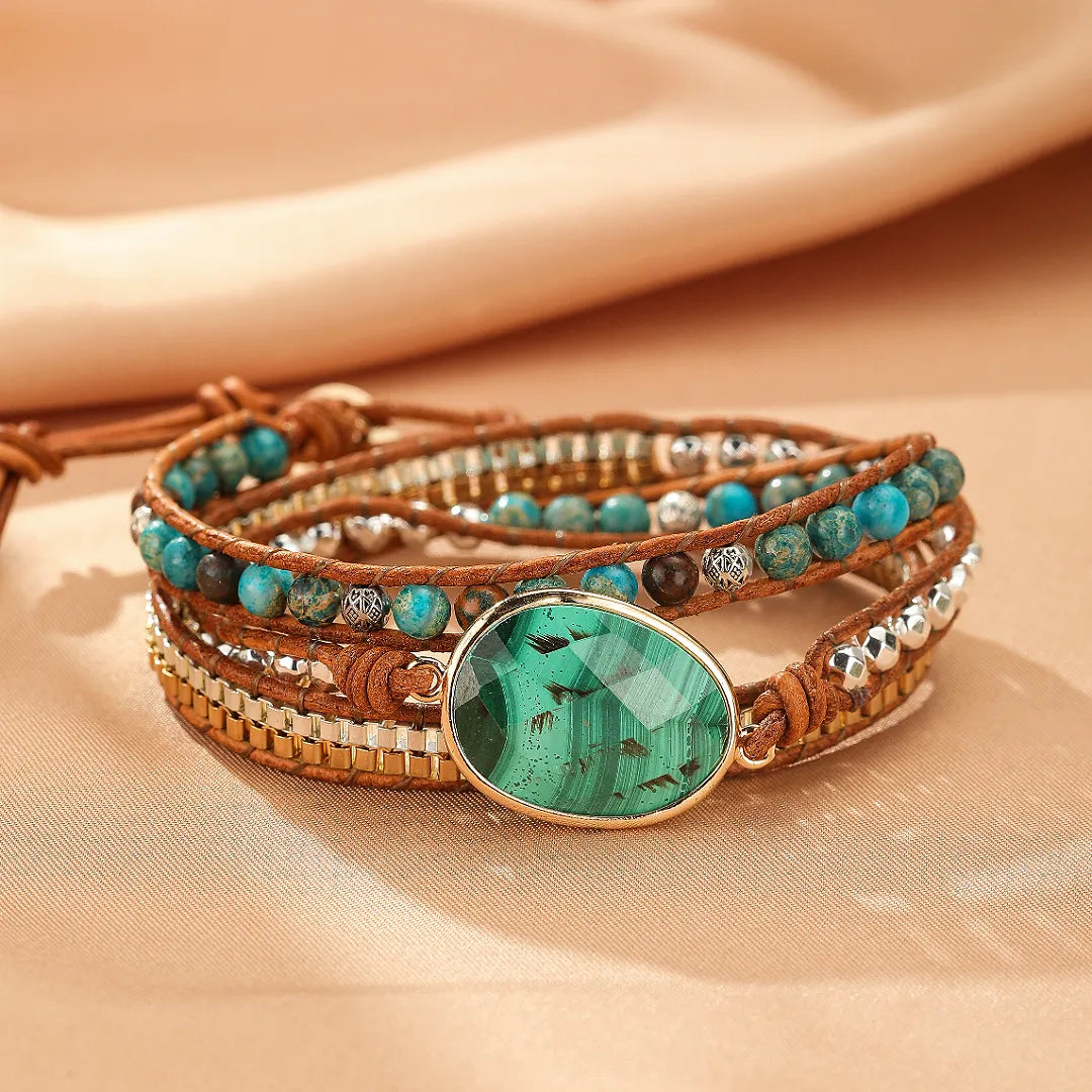 Bracelet jonc enroulé en malachite verte avec des perles bleues et dorées sur un fond beige doux.