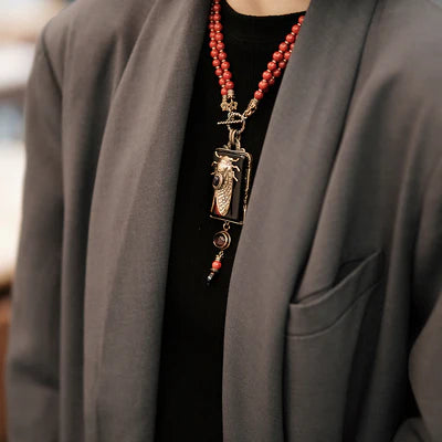 Collier ras du cou avec un pendentif en forme de cigale surmontant une agate noire, porté par une personne vêtue d'une veste grise.