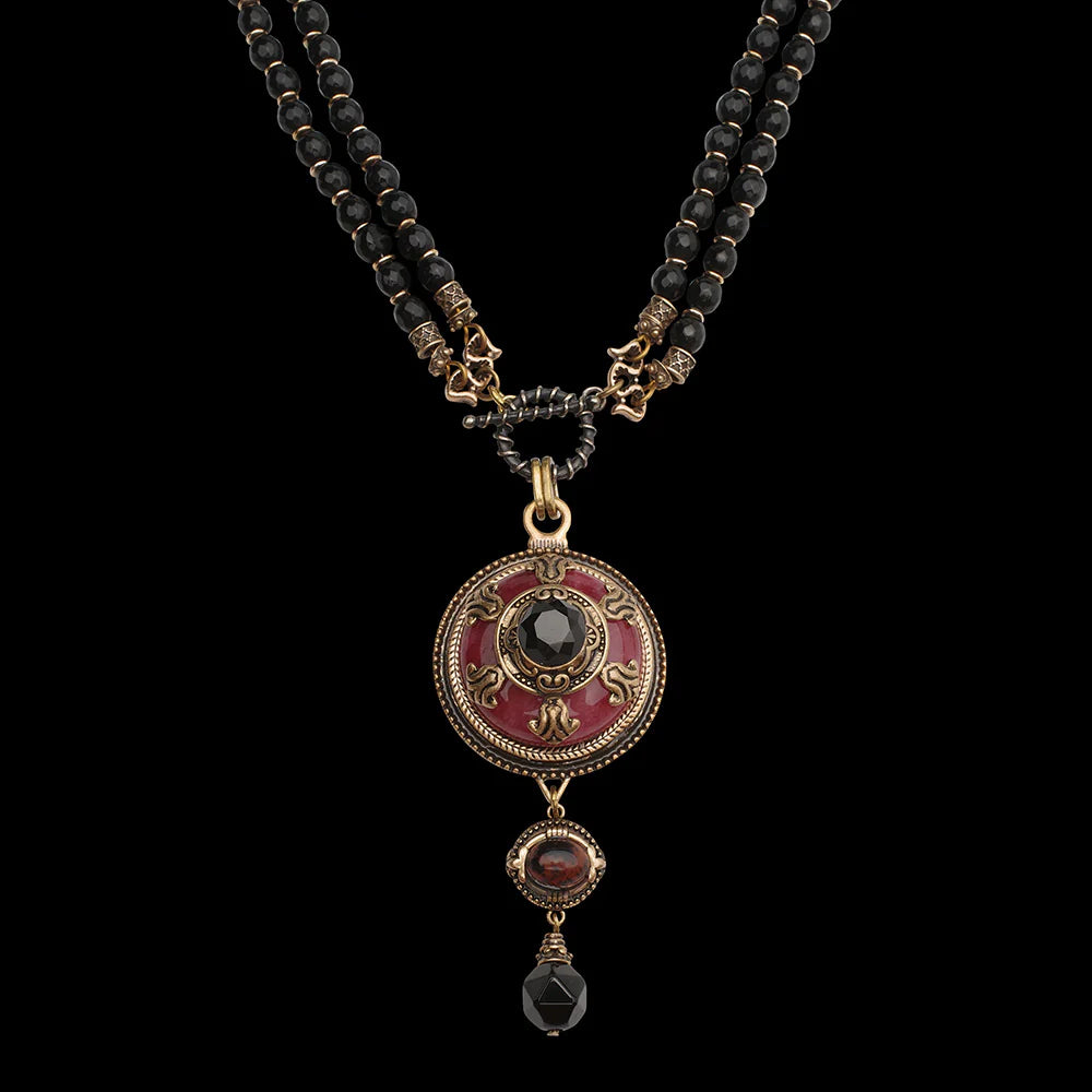 Collier "Merveille d'Antan" avec pendentif rond rouge orné de détails dorés et d'une agate noire centrale, surmontant deux pierres tombantes, le tout monté sur deux rangs de perles noires.