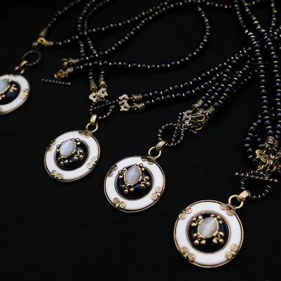 Collier Agate Noire "Pureté Mystique" avec pendentif rond blanc et noir orné d'une pierre centrale pâle et de détails dorés, sur fond noir.