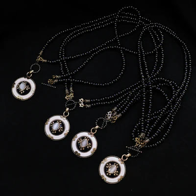 Quatre colliers Agate Noire "Pureté Mystique" avec des pendentifs ronds blancs ornés de pierres ovales claires et de détails dorés.