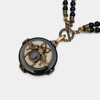 Collier "Reine Noire" avec pendentif rond en agate noire orné d'une abeille dorée et d'une pierre sombre, monté sur une double chaîne de perles noires.