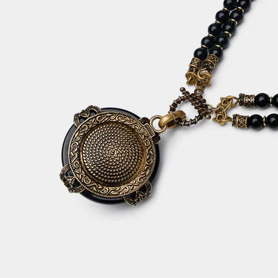 Collier "Reine Noire" avec pendentif rond en agate noire orné d'une gravure dorée en spirale, monté sur deux rangs de perles noires et fermoir mousqueton.