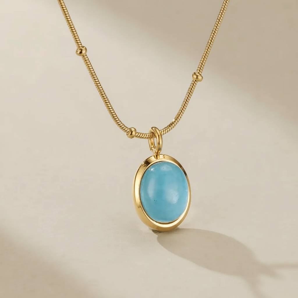 Collier en acier titane doré à l'or 18 carats avec un pendentif ovale bleu aigue-marine "Clarté Céleste".