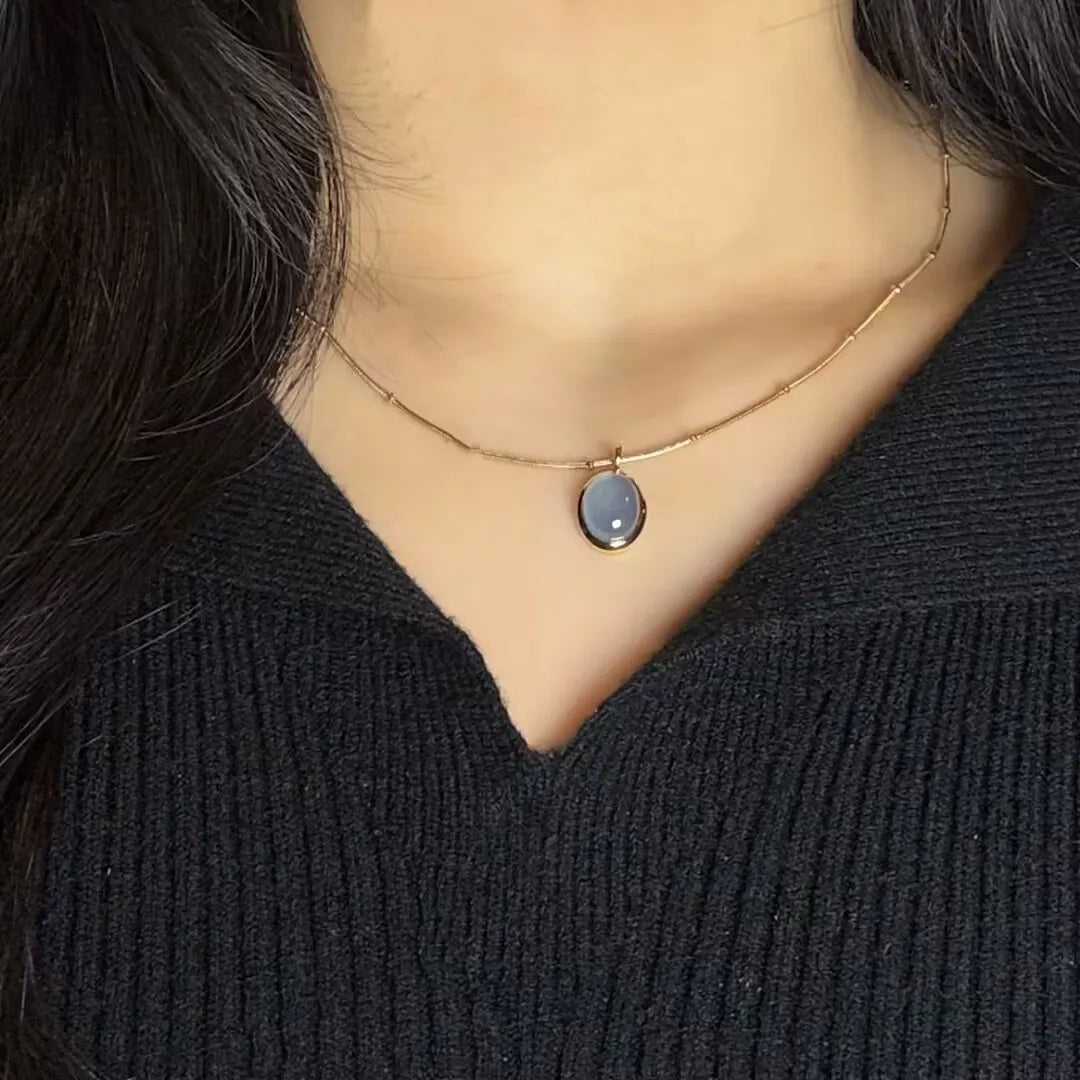 Collier en acier titane doré à l'or 18 carats avec une pierre d'aigue-marine ovale et translucide, porté par une femme.