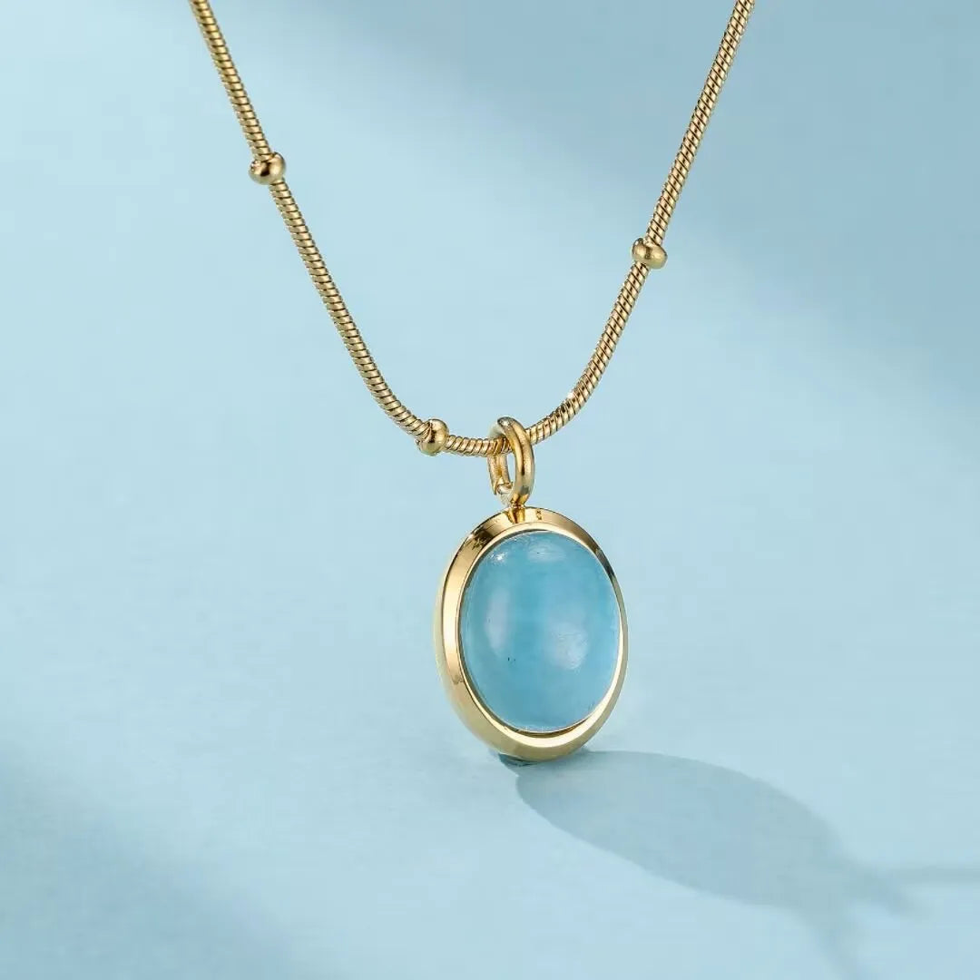 Collier plaqué or avec une pierre d'aigue-marine ovale et bleue ciel, monté sur une chaîne fine dorée avec des petites perles.