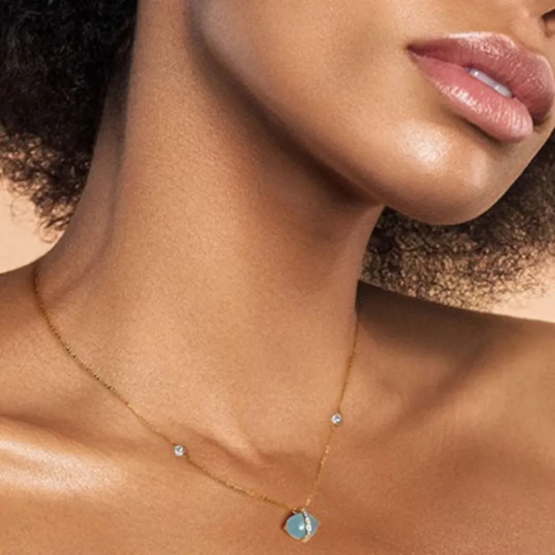 Gros plan sur le collier "Galaxie Bleue" en argent doré or 14K avec une aigue-marine bleue et des diamants sur la peau d'une femme.