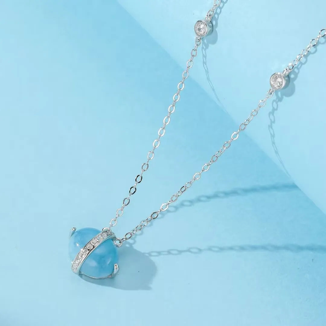 Collier "Galaxie Bleue" avec une pierre d'aigue-marine ronde et bleue, sertie sur une monture en argent 925 doré à l'or 14 carats, ornée de petites pierres scintillantes.
