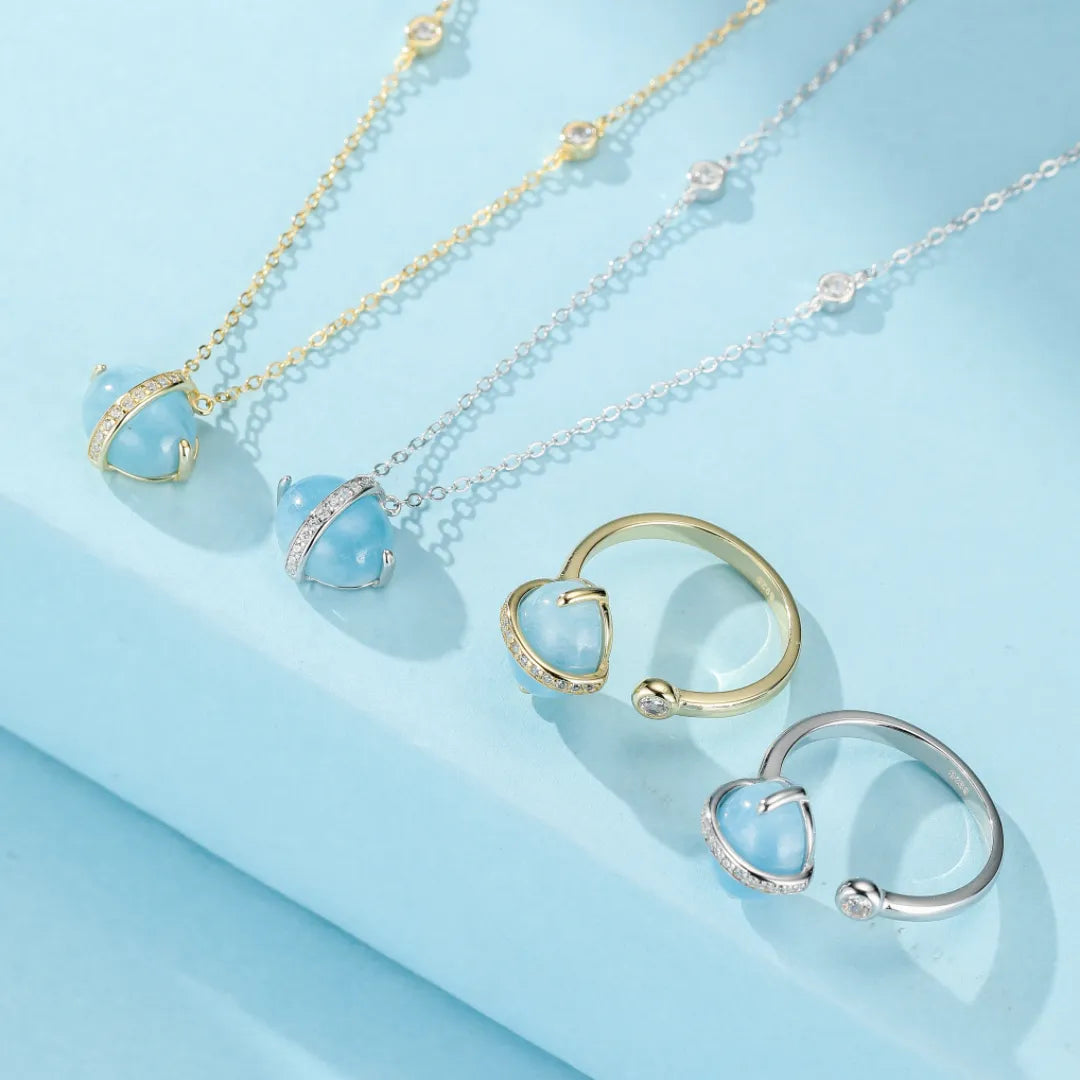 Ensemble de bijoux en argent doré or 14K avec des pendentifs et bagues en forme de cœur en aigue-marine bleue, ornés de petites pierres scintillantes.