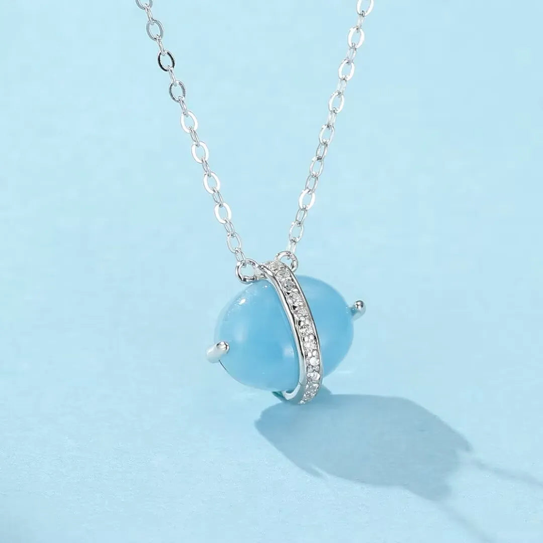 Collier "Galaxie Bleue" avec une pierre d'aigue-marine ovale bleue et une bande d'argent dorée sertie de zircons cubiques, suspendu à une chaîne en argent.