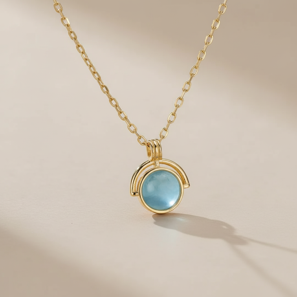 Collier "Mystère d'Océan" en argent 925 avec une pierre d'aigue-marine bleue ronde et lumineuse, suspendu à une fine chaîne dorée.