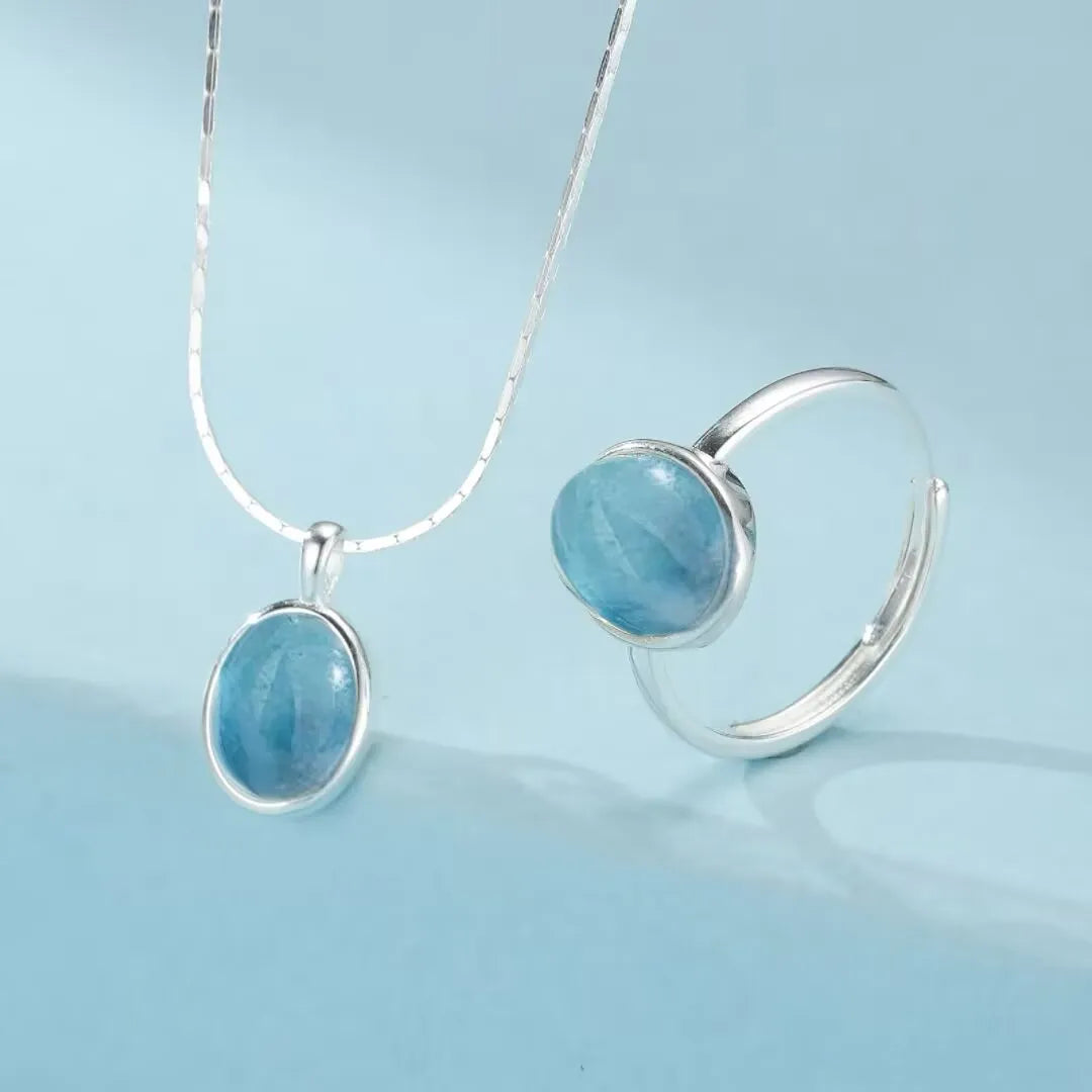 Ensemble de bijoux "Pureté Profonde" en argent 925, comprenant un collier avec un pendentif ovale en aigue-marine et une bague assortie avec une pierre d'aigue-marine ovale.