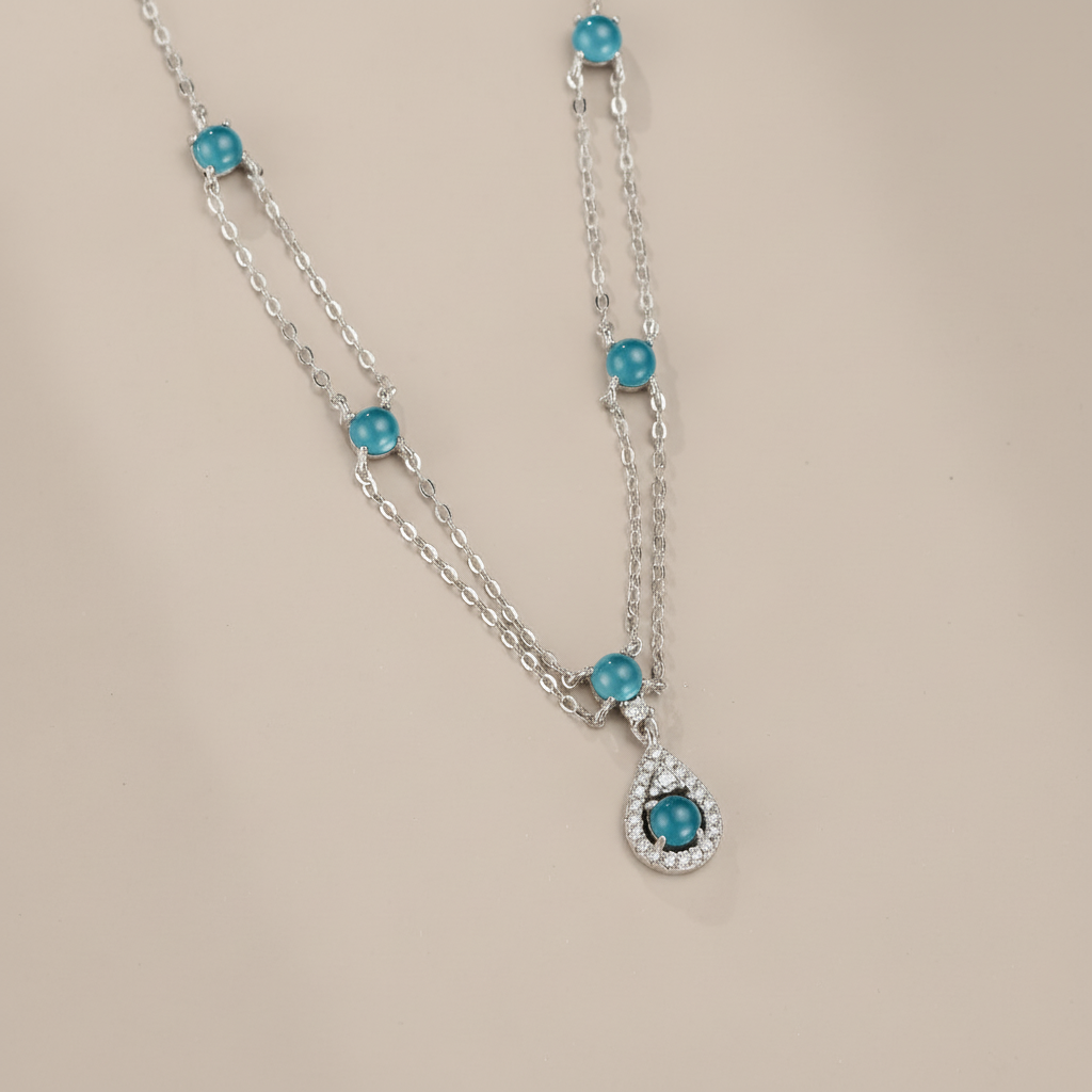 Collier double chaîne en argent orné de petites pierres rondes d'aigue-marine bleues et d'un pendentif en forme de goutte serti de cristaux et d'une aigue-marine centrale.
