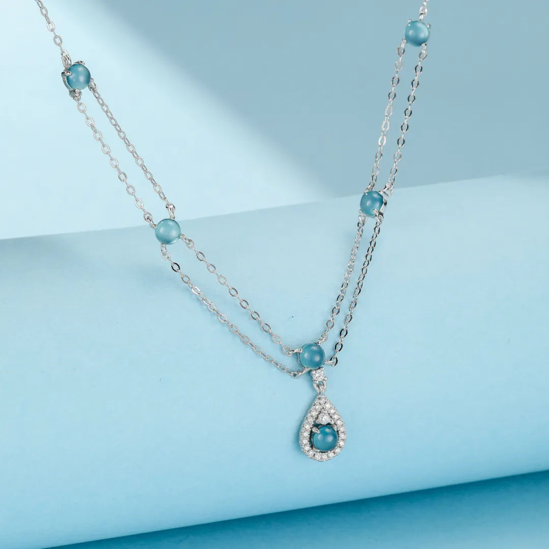 Collier Aigue Marine "Sirène Magique" en argent, double chaîne ornée de petites perles bleues et d'un pendentif goutte serti de zircons.