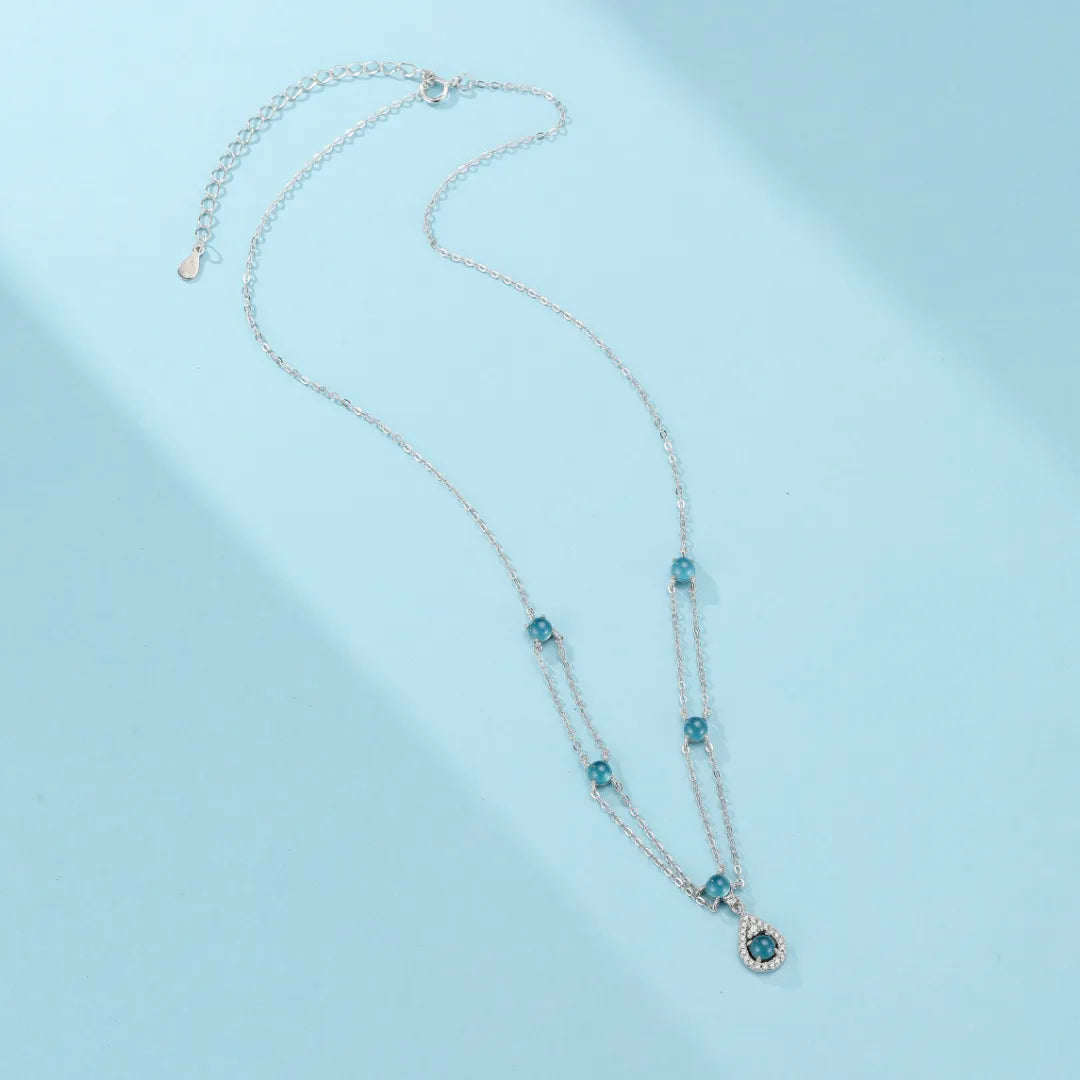 Collier en argent avec des perles d'aigue-marine bleues et un pendentif en forme de goutte orné de cristaux scintillants.
