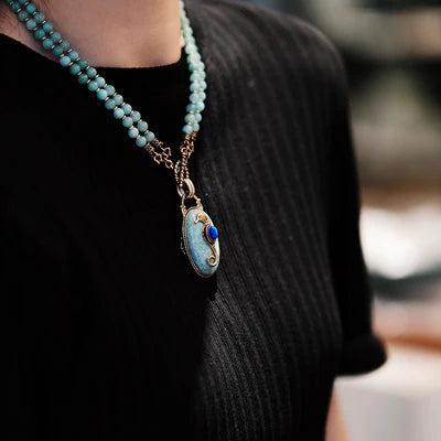 Collier "Voyage Marin" avec pendentif en amazonite et petite pierre bleue en forme d'hippocampe, porté sur un haut noir.