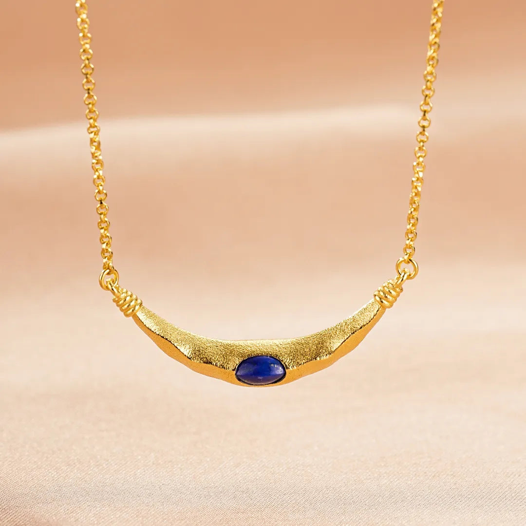 Collier ras du cou en argent doré avec une pierre de lapis-lazuli bleue ovale au centre sur un fond rose pâle fond beige
