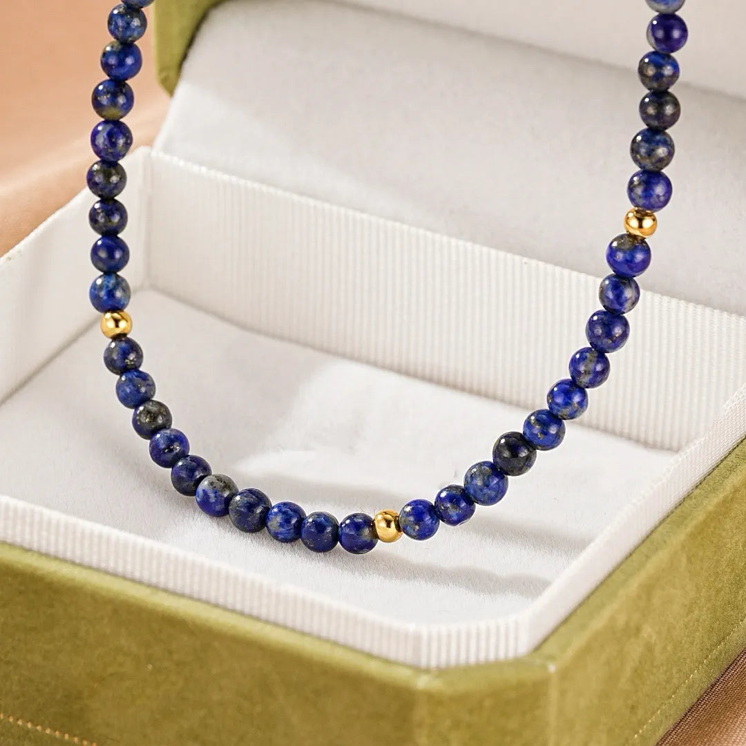 Collier "Beauté Astrale" fait de perles de lapis-lazuli bleu profond et de petites perles dorées, présenté dans un écrin vert.