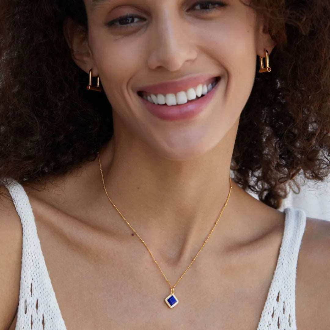 Gros plan sur un collier "Élégance Raffinée" en argent doré avec un pendentif carré bleu lapis-lazuli, porté par une femme souriante.